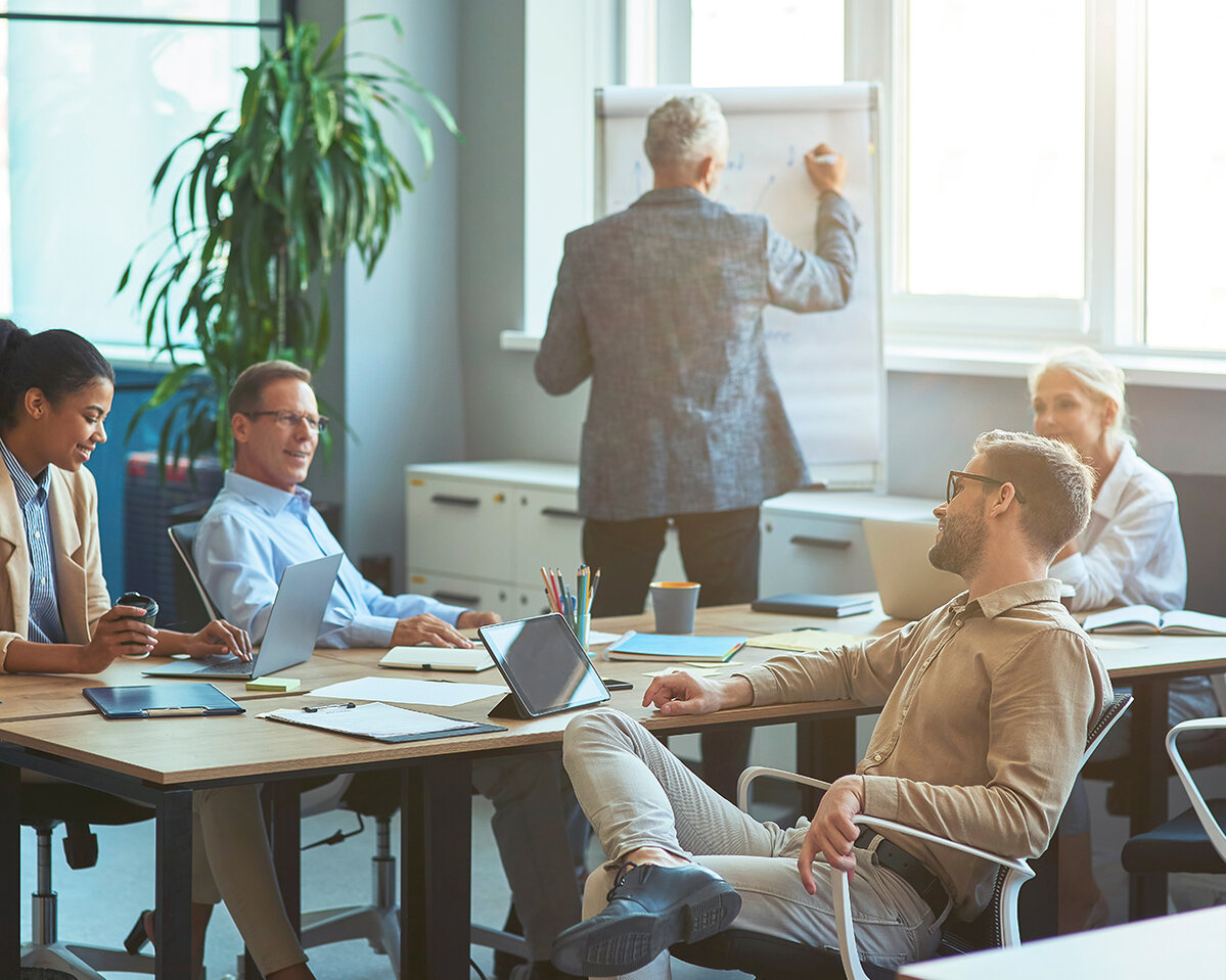 Mann, der etwas an eine weiße Tafel schreibt und ein Brainstorming mit seinem Team in einem modernen Büro oder Coworking Space abhält. Business Menschen arbeiten zusammen
