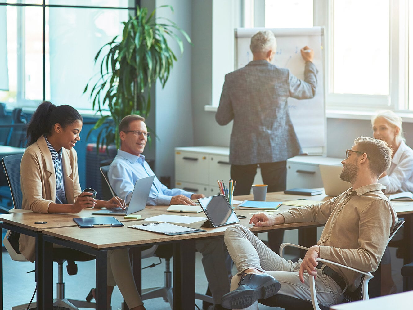 Mann, der etwas an eine weiße Tafel schreibt und ein Brainstorming mit seinem Team in einem modernen Büro oder Coworking Space abhält. Business Menschen arbeiten zusammen