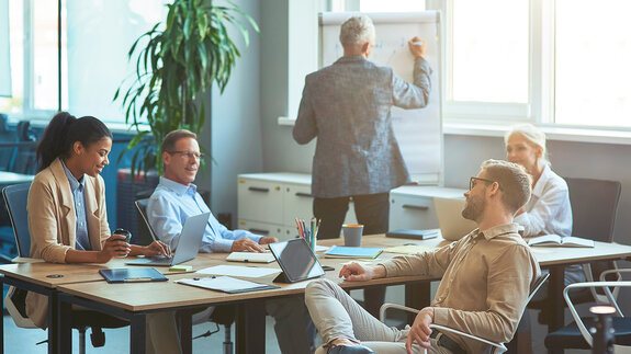 Mann, der etwas an eine weiße Tafel schreibt und ein Brainstorming mit seinem Team in einem modernen Büro oder Coworking Space abhält. Business Menschen arbeiten zusammen