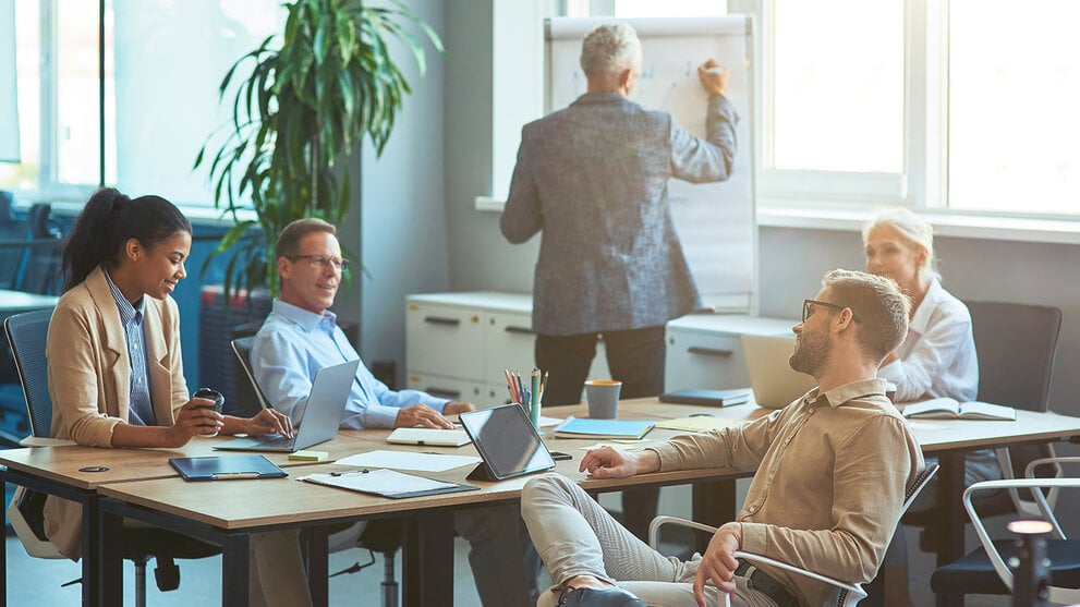Mann, der etwas an eine weiße Tafel schreibt und ein Brainstorming mit seinem Team in einem modernen Büro oder Coworking Space abhält. Business Menschen arbeiten zusammen