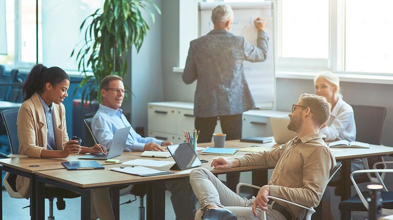 Mann, der etwas an eine weiße Tafel schreibt und ein Brainstorming mit seinem Team in einem modernen Büro oder Coworking Space abhält. Business Menschen arbeiten zusammen