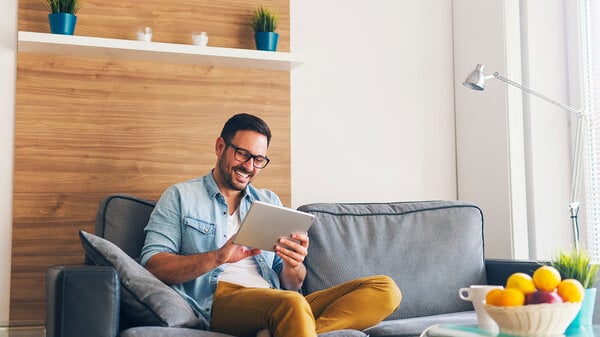 Mann mit Brille auf der Couch in modernem Wohnzimmer nutzt das Tablet
