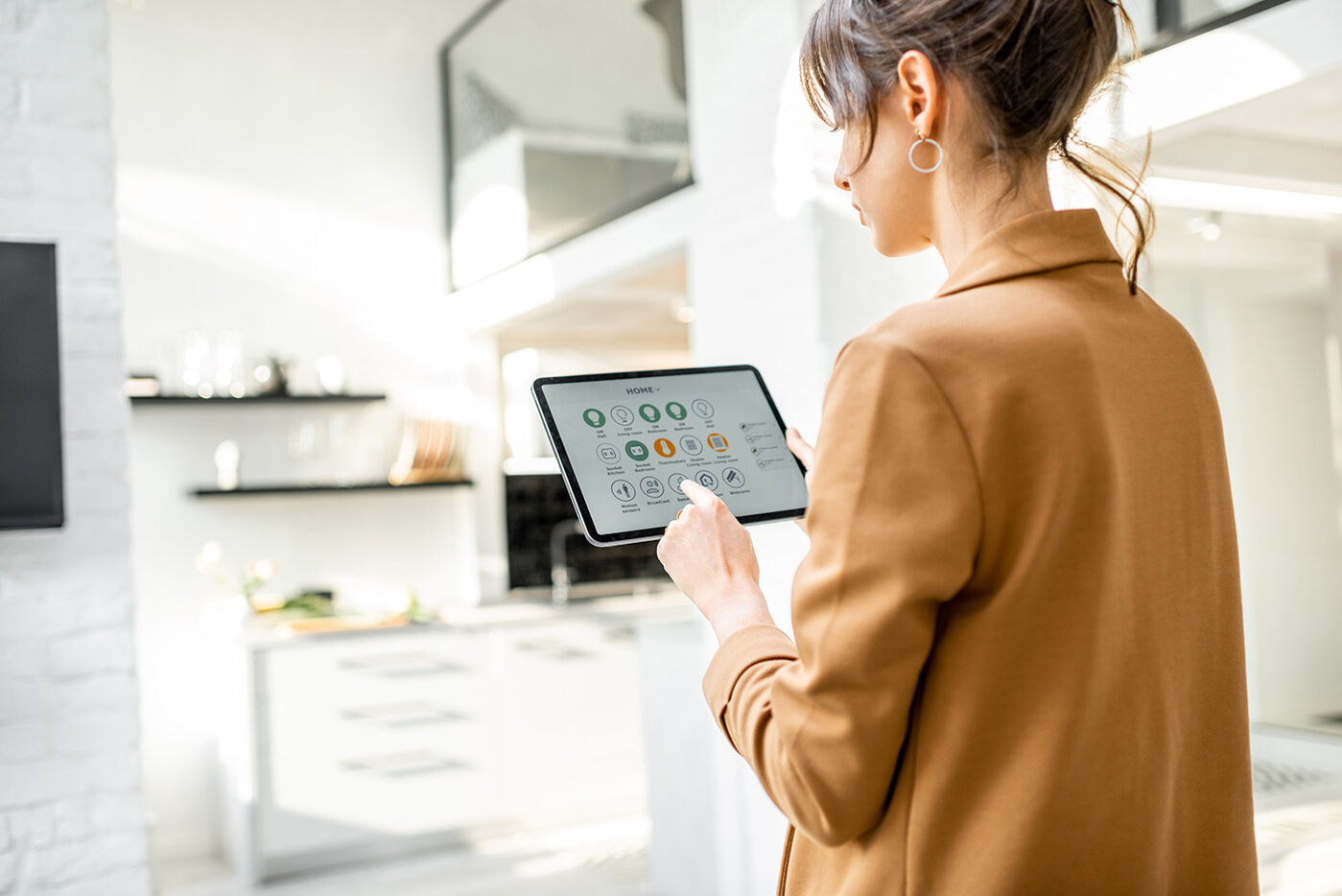 Eine Frau steuert im weißen Wohnzimmer Smart-Home-Geräte über ein Tablet mit einer darauf installierten App. Smart-Home-Konzept 