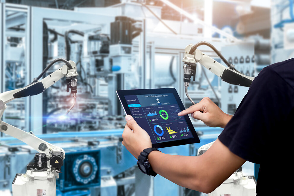  Intelligentes Steuerungskonzept für die Industrie. Hände, die ein Tablet halten, vor dem Hintergrund einer verschwommenen Automatisierungsmaschine 