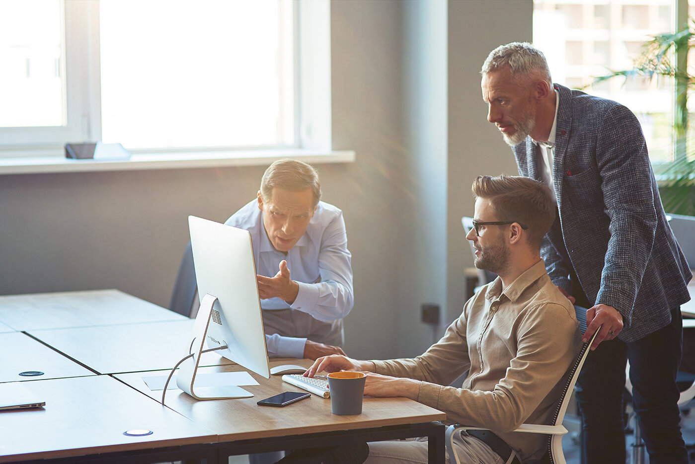 Drei männliche Mitarbeiter, die auf einen PC-Bildschirm schauen und ein Projekt besprechen, Geschäftsleute, die im Coworking Space zusammenarbeiten