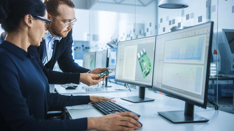  Moderne Elektronikfabrik: Ein männlicher Vorgesetzter spricht mit einer Elektroingenieurin, die am Computer mit CAD-Software arbeitet. Entwicklung von Leiterplatten, Mikrochips, Halbleitern und Telekommunikationsgeräten 
