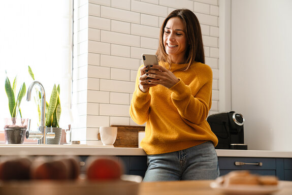 Frau lächelnd und mit Handy in der Wohnung