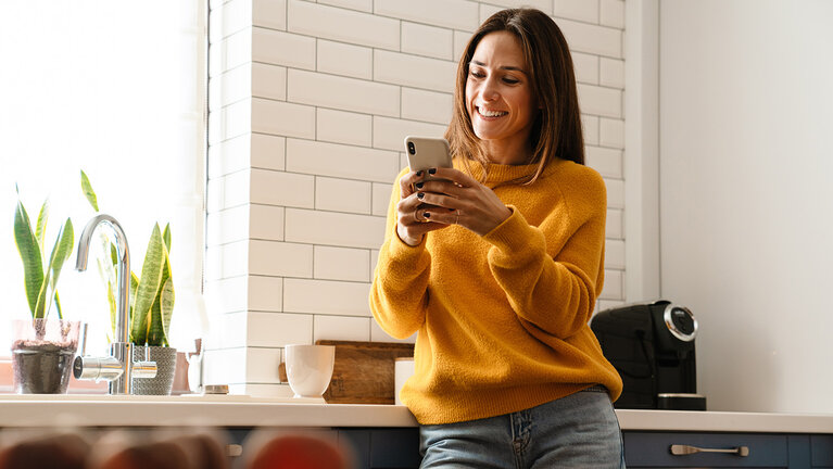 Frau lächelnd und mit Handy in der Wohnung