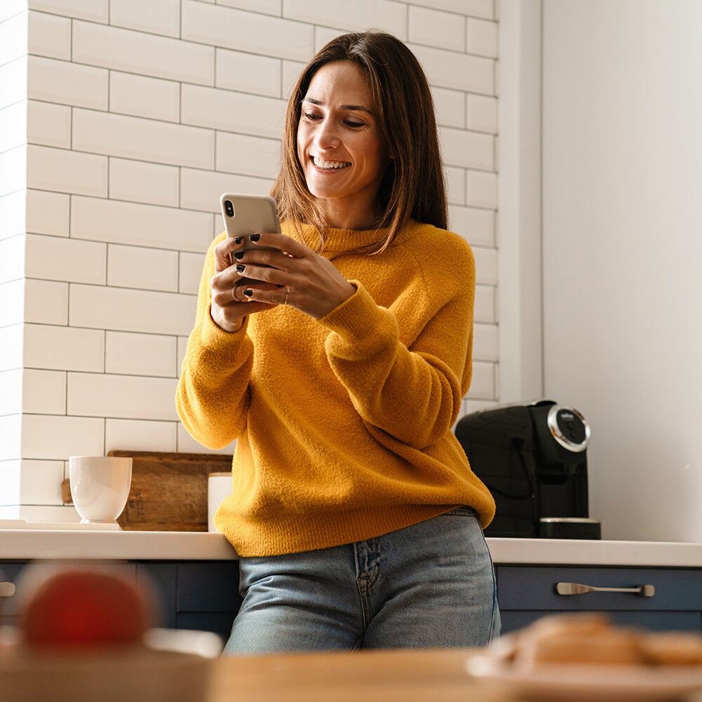 Frau lächelnd und mit Handy in der Wohnung