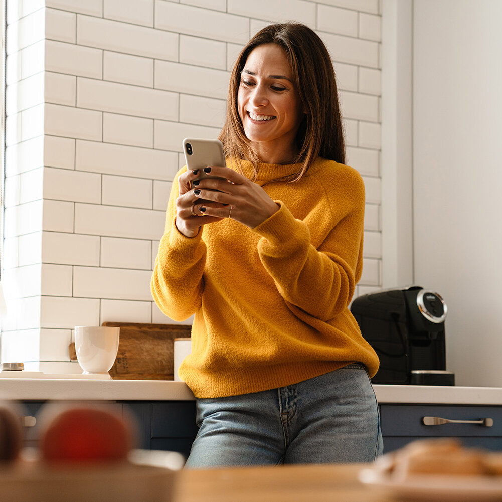 Frau lächelnd und mit Handy in der Wohnung