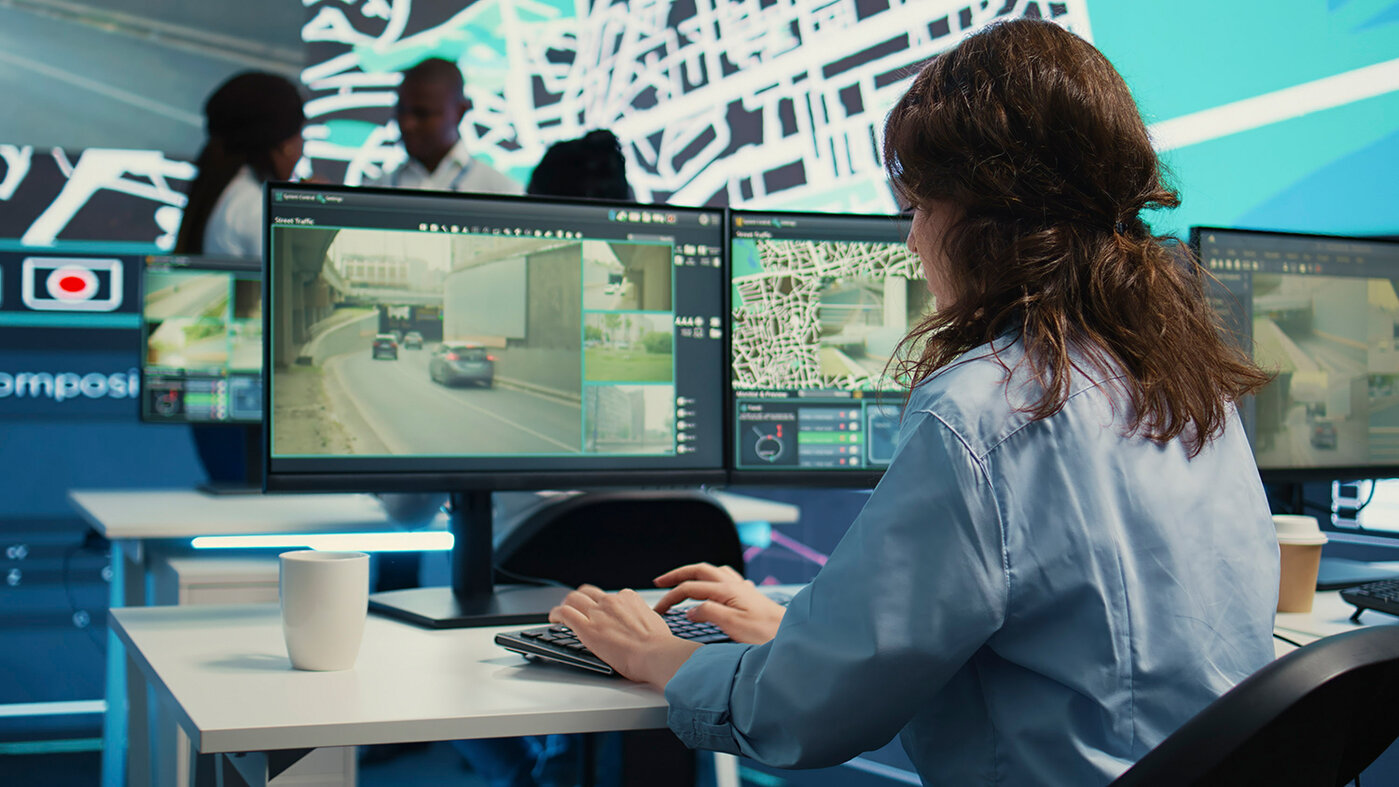 Ein vielfältiges Team von Mitarbeitern, das mithilfe von Karten und Überwachungsaufnahmen die Routen der Lieferwagen in der Stadt überwacht. Mitarbeiter, die mit GPS-Koordinaten arbeiten, um Bestellungen und die Frachtlogistik zu verfolgen. Kamera B. 