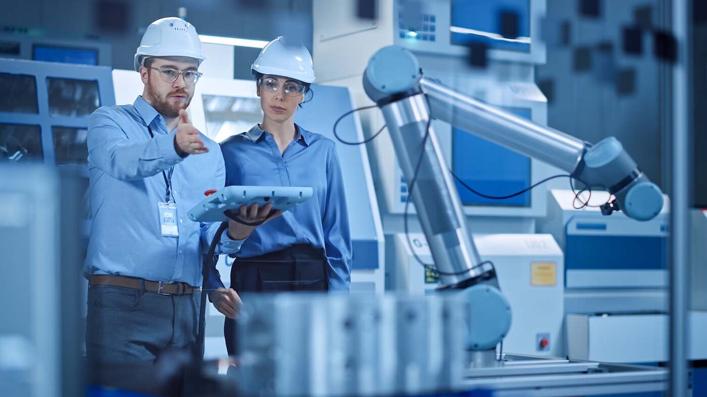 Werkstatt: Eine professionelle Ingenieurin und ein Maschinenbediener nutzen industrielle Tablet-Computer, um zu arbeiten und einen Roboterarm für die Produktionslinie zu programmieren. Hightech-Anlage mit CNC-Maschinen 