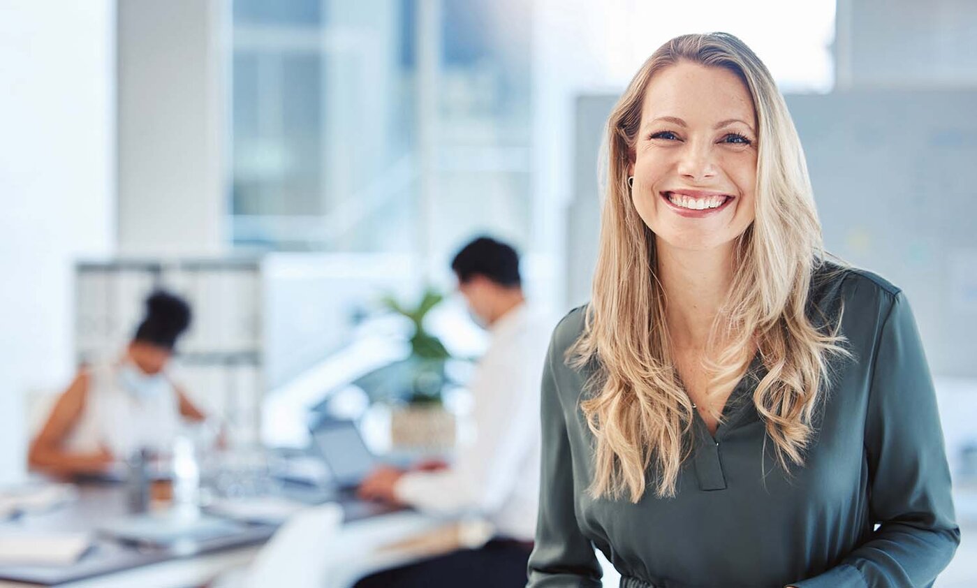 Eine weibliche Führungskraft, Managerin oder Geschäftsführerin mit einem Lächeln, einer Mission und einer Vision im Büro, im Hintergrund ihr Team. Führung, Management und Erfolg mit einer Chefin und Geschäftsleuten bei der Arbeit