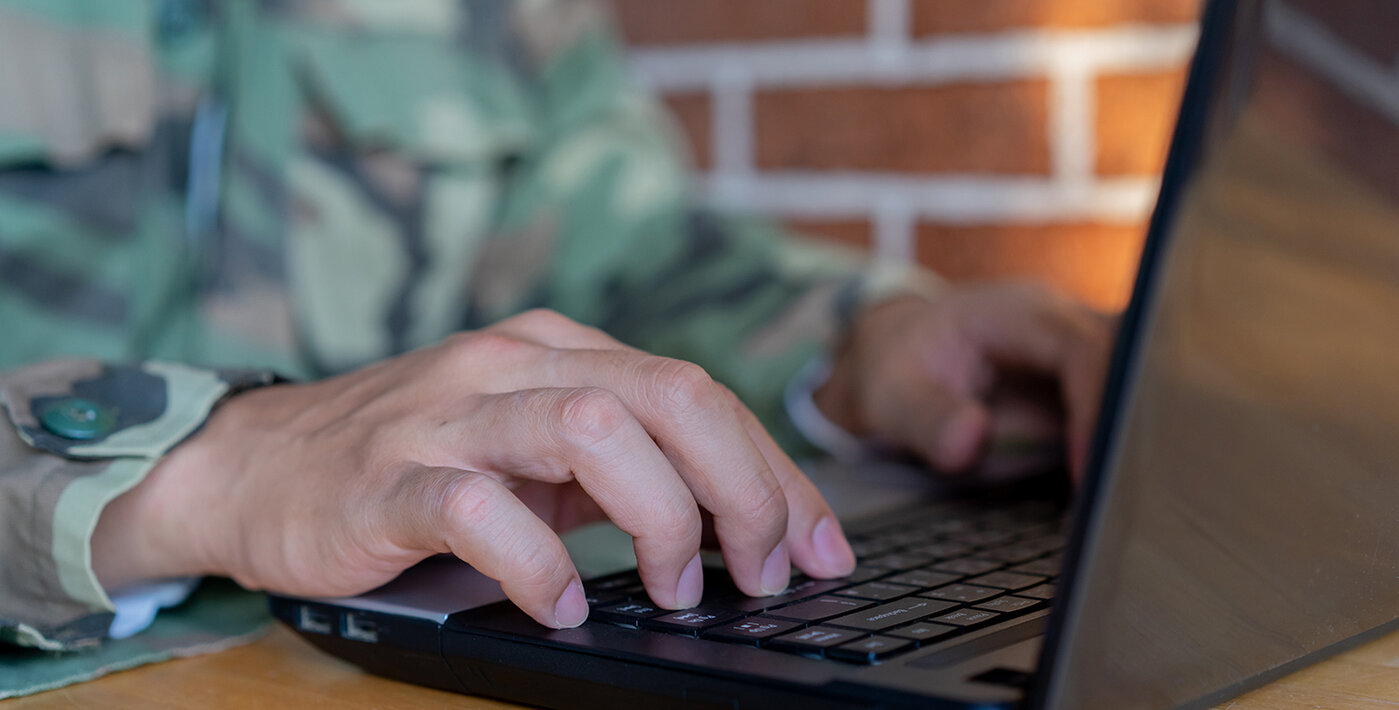  Nahaufnahme eines Soldaten, der an einem Laptop auf der Tastatur tippt, um Befehle für ein Testsystem für militärische Operationen in einem Büro zu überprüfen und einzugeben
