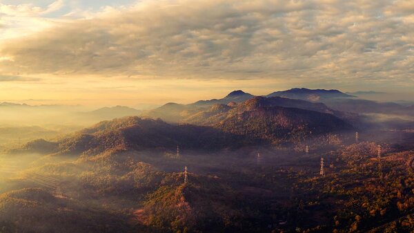 Luftaufnahme: Panorama eines malerischen Morgenbildes in den hohen Bergen mit Strommast in Pang Puay, Mae Moh, Lampang, Thailand. Ein wunderschöner Morgen mit goldenem Sonnenaufgang und wogendem Nebel.
