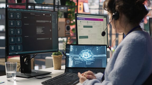  Mitarbeiter im Live-Chat-Support, der auf der Tastatur tippt und einen KI-Chatbot nutzt, um Kundenbeschwerden zu bearbeiten. Callcenter-Mitarbeiter, der sich mithilfe von künstlicher Intelligenz (LLM) und einer Kamera um unzufriedene Kunden kümmert