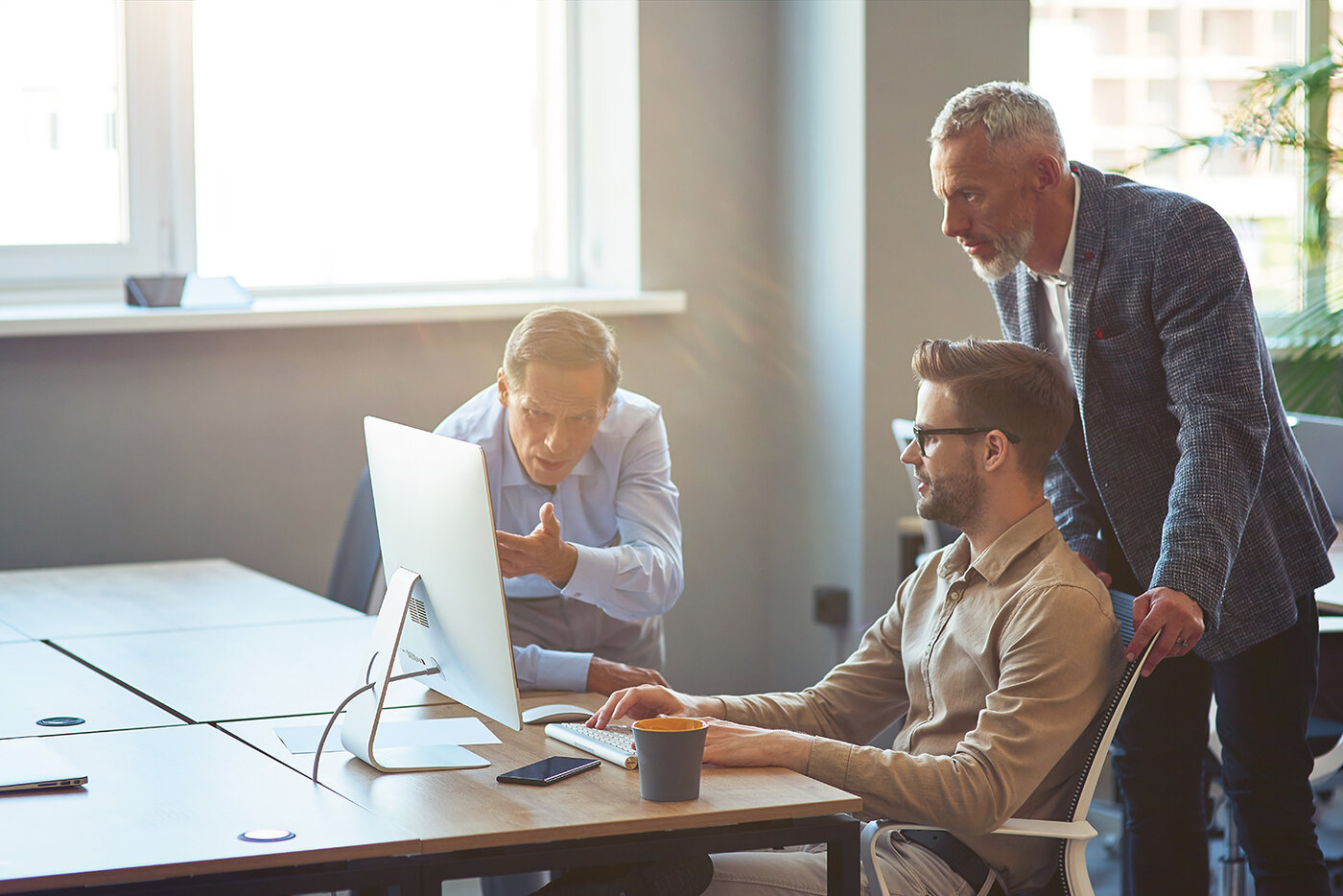 Drei männliche Mitarbeiter, die auf einen PC-Bildschirm schauen und ein Projekt besprechen, Geschäftsleute, die im Coworking Space zusammenarbeiten