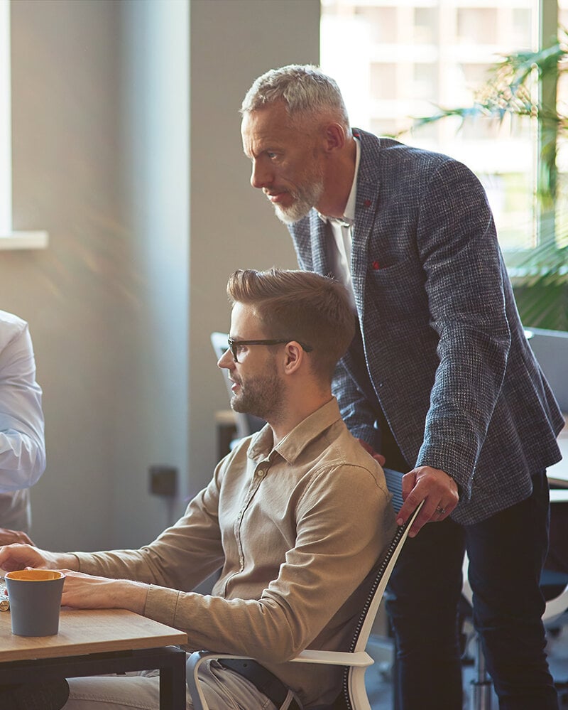 Drei männliche Mitarbeiter, die auf einen PC-Bildschirm schauen und ein Projekt besprechen, Geschäftsleute, die im Coworking Space zusammenarbeiten