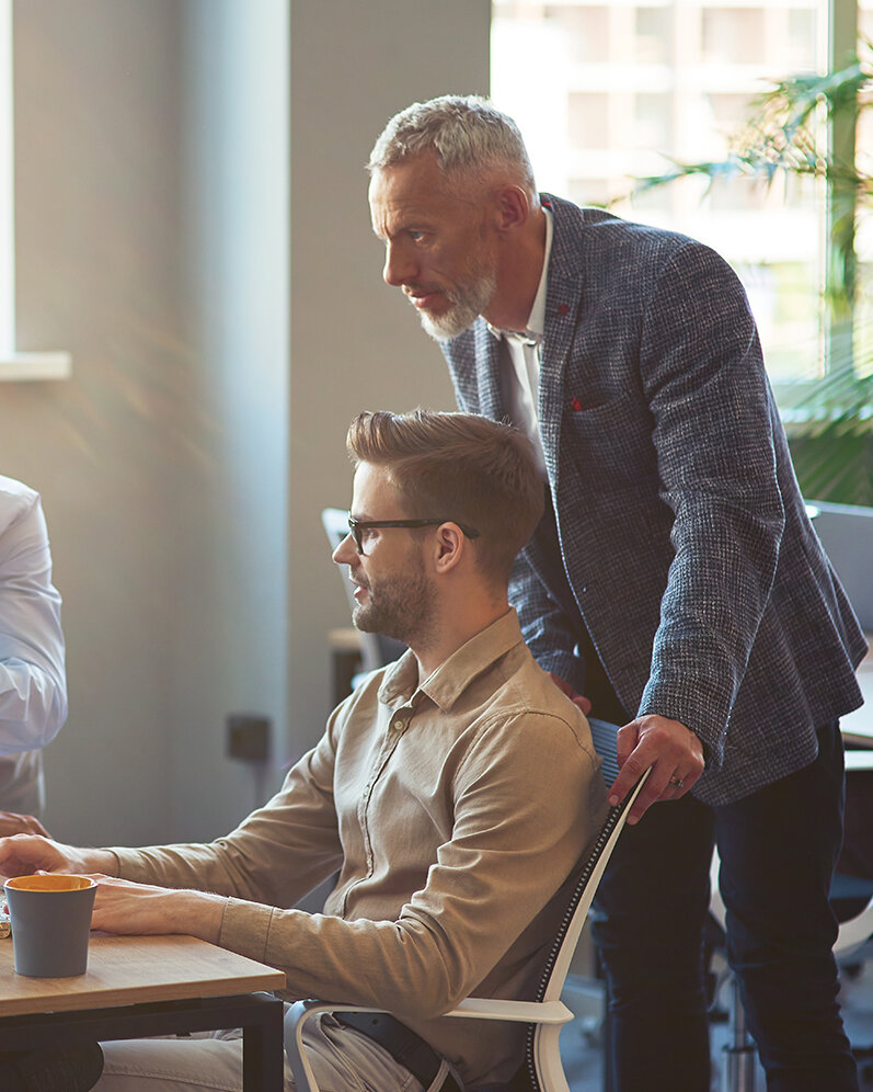Drei männliche Mitarbeiter, die auf einen PC-Bildschirm schauen und ein Projekt besprechen, Geschäftsleute, die im Coworking Space zusammenarbeiten