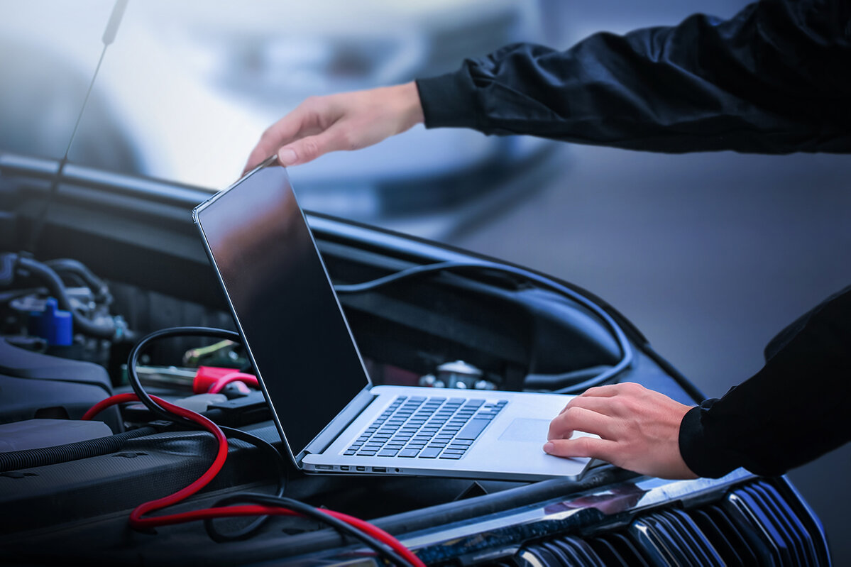Computerdiagnose des Fahrzeugs in der Werkstatt. Kfz-Mechaniker, der mit einem Laptop programmiert und Diagnosesoftware für Fahrzeuge einsetzt, sowie das Konzept der Fahrzeugwartung.