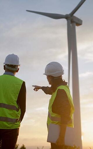 Ingenieure überprüfen den Betrieb eines Windkraftwerks, besprechen bei Sonnenuntergang die Strategie für ein Projekt im Bereich erneuerbare Energien und gestalten so eine nachhaltige Zukunft