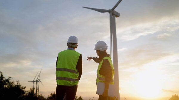Ingenieure überprüfen den Betrieb eines Windkraftwerks, besprechen bei Sonnenuntergang die Strategie für ein Projekt im Bereich erneuerbare Energien und gestalten so eine nachhaltige Zukunft
