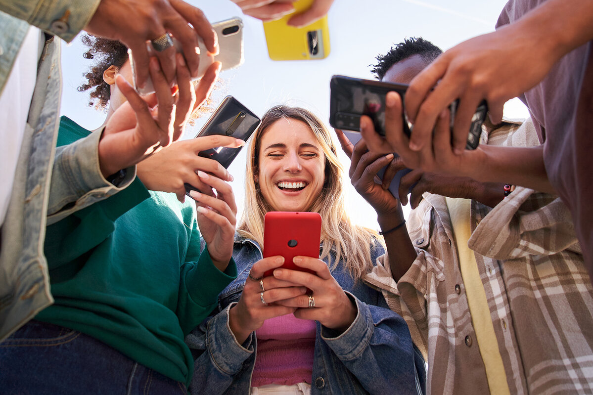 Niedriger Winkel Blick auf eine Gruppe von jungen Teenagern Freunde mit Handys und zu Fuß in der Stadt. Konzept der Gemeinschaft Millennial Menschen süchtig nach Technologie. Social Media Kommunikation Generation Z
