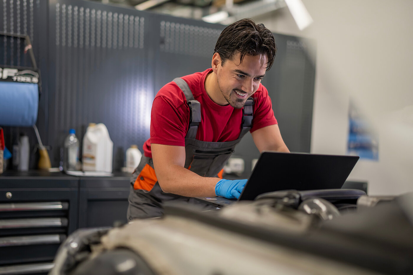 Mechaniker, der in einer Werkstatt mithilfe eines Laptops eine Diagnose am Automotor durchführt 