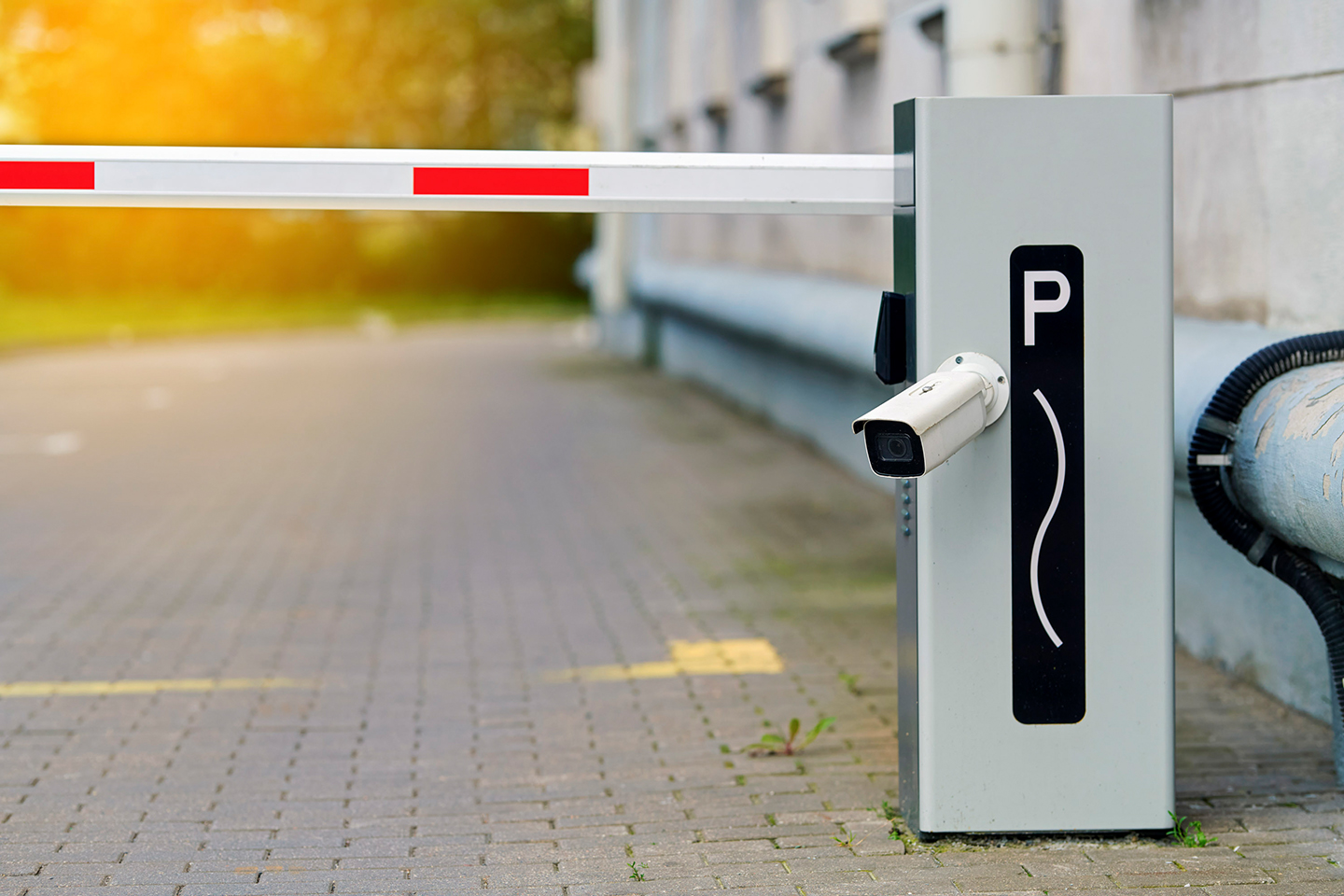 Automatische Schrankenanlage für die Parkplatzverwaltung mit Überwachungskamera. Automatisches Sicherheitstor mit gestreiftem Schrankenarm und integrierter Überwachungskamera, das den Zugang zum privaten Parkplatzbereich beschränkt